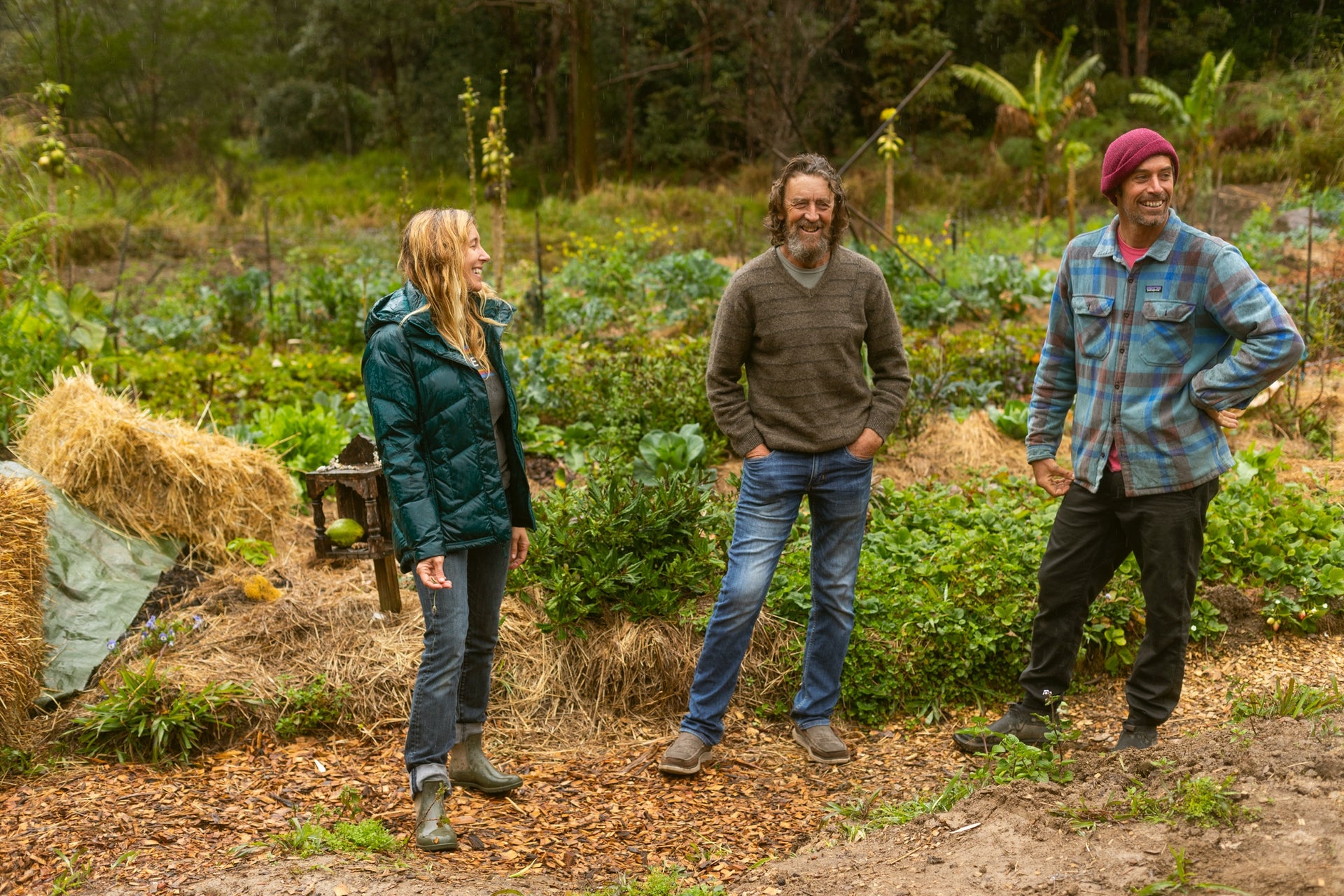Lauren Hill and Dave Rastovich standing with Geoff Lawton (centre) in their community permaculture garden on the NSW North Coast. Photo: Nathan Oldfield